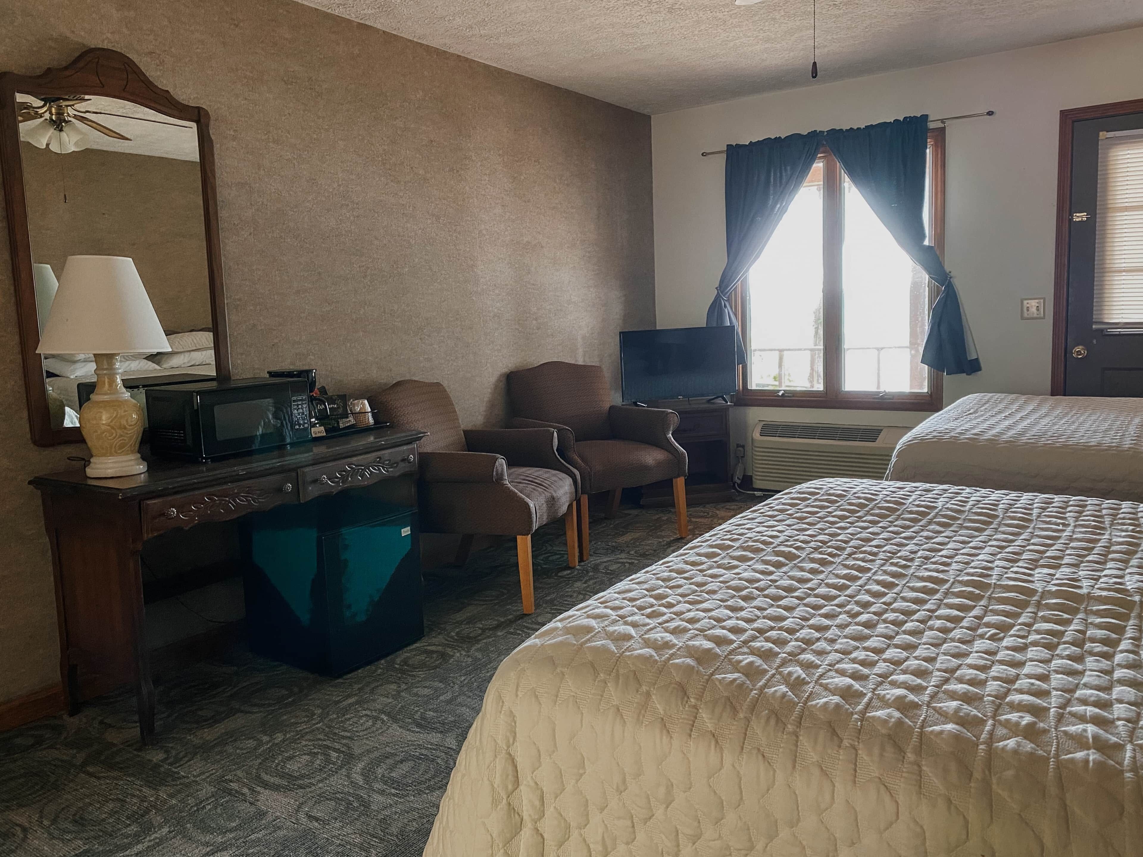 A hotel room with a bed, a desk with a lamp, a chair, a television, and a window with curtains.