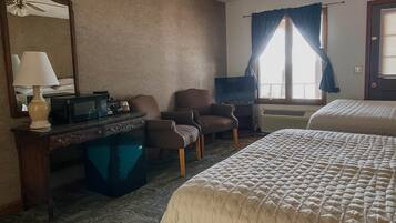A hotel room with a bed, a desk with a lamp, a chair, a television, and a window with curtains.