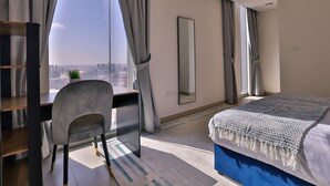 Ein modernes Hotelzimmer mit großem Fenster, Schreibtisch, Stuhl, Bett und Spiegel.