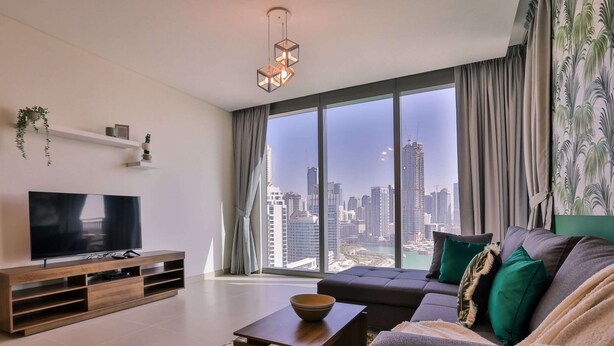Ein modernes Wohnzimmer mit großem Fernseher, einer Holzunterhaltungsecke, einer Couch mit Kissen, einem Couchtisch und Blick auf eine Stadtlandschaft durch große Fenster.