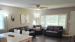 A living room with a white table, two leather couches, a ceiling fan, and a window with blinds. - Modern 3BD/2BA near U of I with a large master suite! (Champaign)