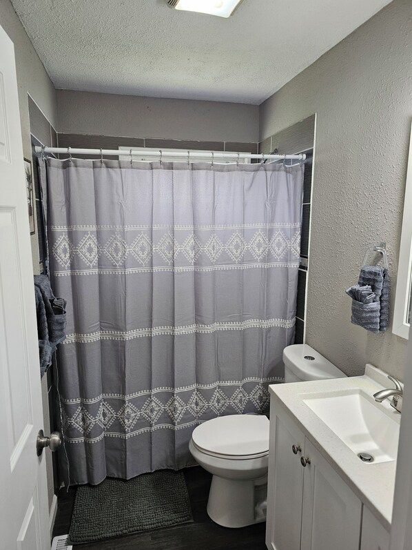 Un baño con cortina de ducha, inodoro, lavabo y perchero.