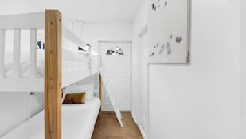 A bunk bed room with a wooden ladder, white walls, and a door with a window.