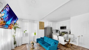 Una sala de estar moderna con un sofá azul, una mesa de centro de vidrio y una zona de comedor con sillas blancas y una mesa de vidrio.
