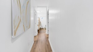 Un pasillo con paredes blancas y suelo de madera que conduce a una habitación con una cama y un ventanal.