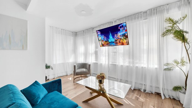 Una sala de estar moderna con una mesa de centro de vidrio, un sofá color turquesa y un televisor que muestra una escena colorida.