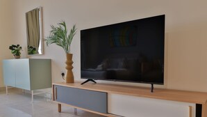 En moderne stue med et fladskærms-tv ophængt på et træ tv-møbel, et lyst skab med en plante og et stort spejl på væggen.