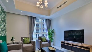 Ein modernes Wohnzimmer mit einer Couch, Sesseln, einem Couchtisch, einem Fernseher und einer Pflanze.