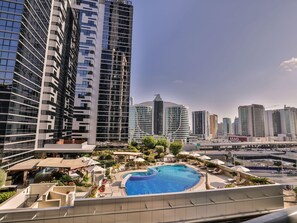 A modern hotel with a rooftop pool, surrounded by high-rise buildings and a clear sky.