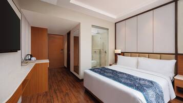 Una habitación de hotel con una cama, una mesita de noche y un televisor a la izquierda.