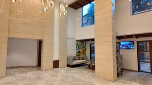 Eine geräumige Lobby mit hohen Decken, einem großen Wandgemälde, einer Sitzecke und einem Fernseher, der eine Karte zeigt.