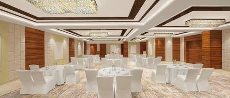 Un amplio salón de banquetes con varias mesas redondas y sillas blancas, que cuenta con un piso de mármol pulido y elegantes candelabros.