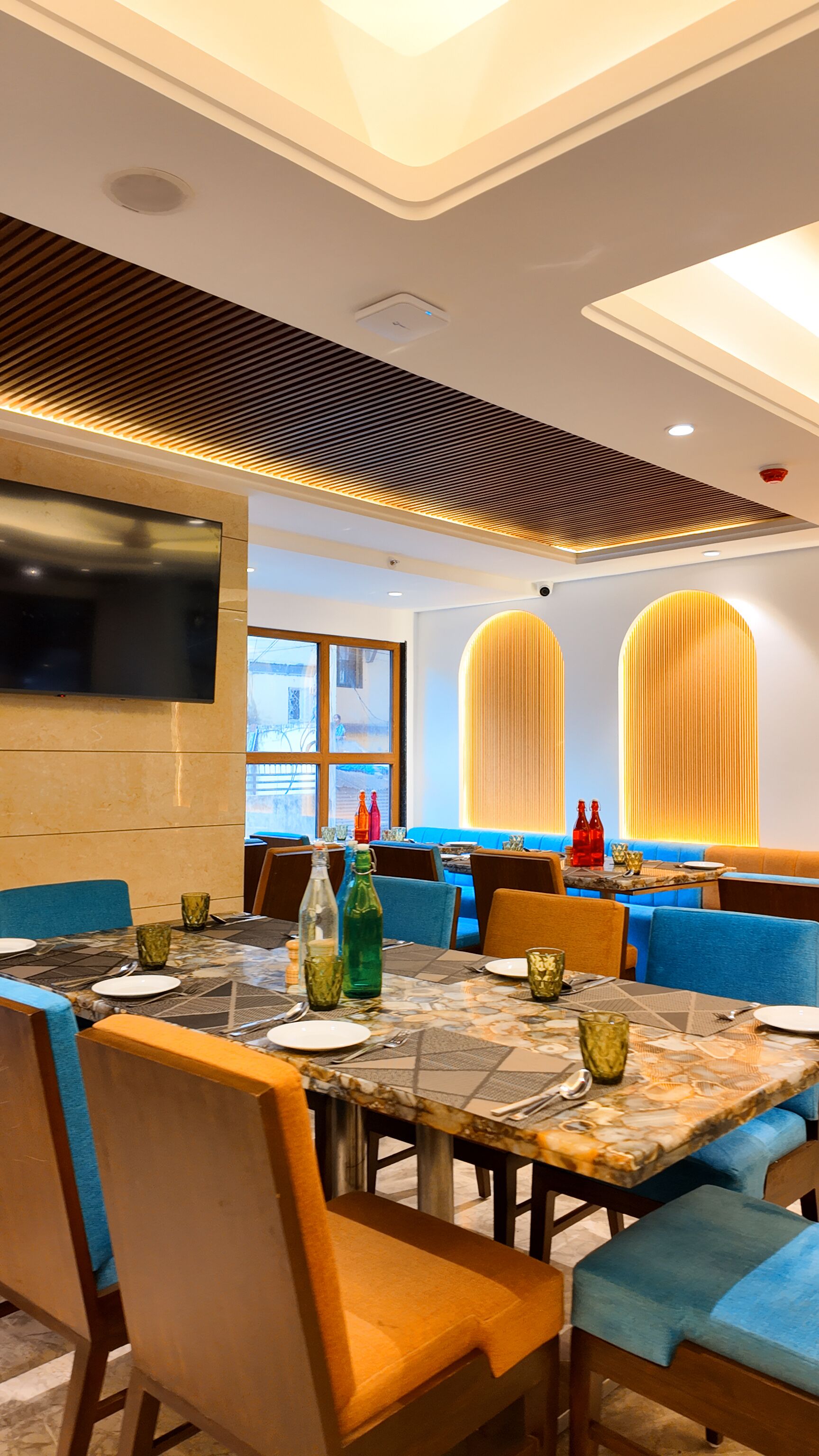 A restaurant with a modern interior, featuring a large dining table, blue cushioned seating, and a flat-screen TV mounted on the wall.