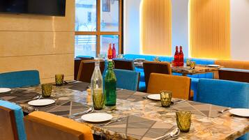 A restaurant with a modern interior, featuring a large dining table, blue cushioned seating, and a flat-screen TV mounted on the wall.