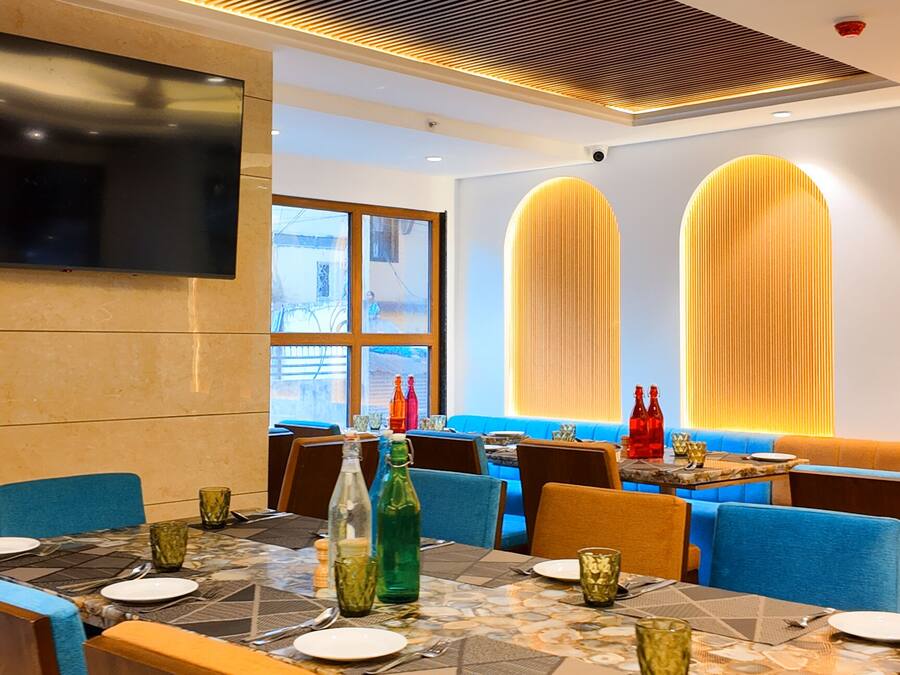 A restaurant with a modern interior, featuring a large dining table, blue cushioned seating, and a flat-screen TV mounted on the wall.