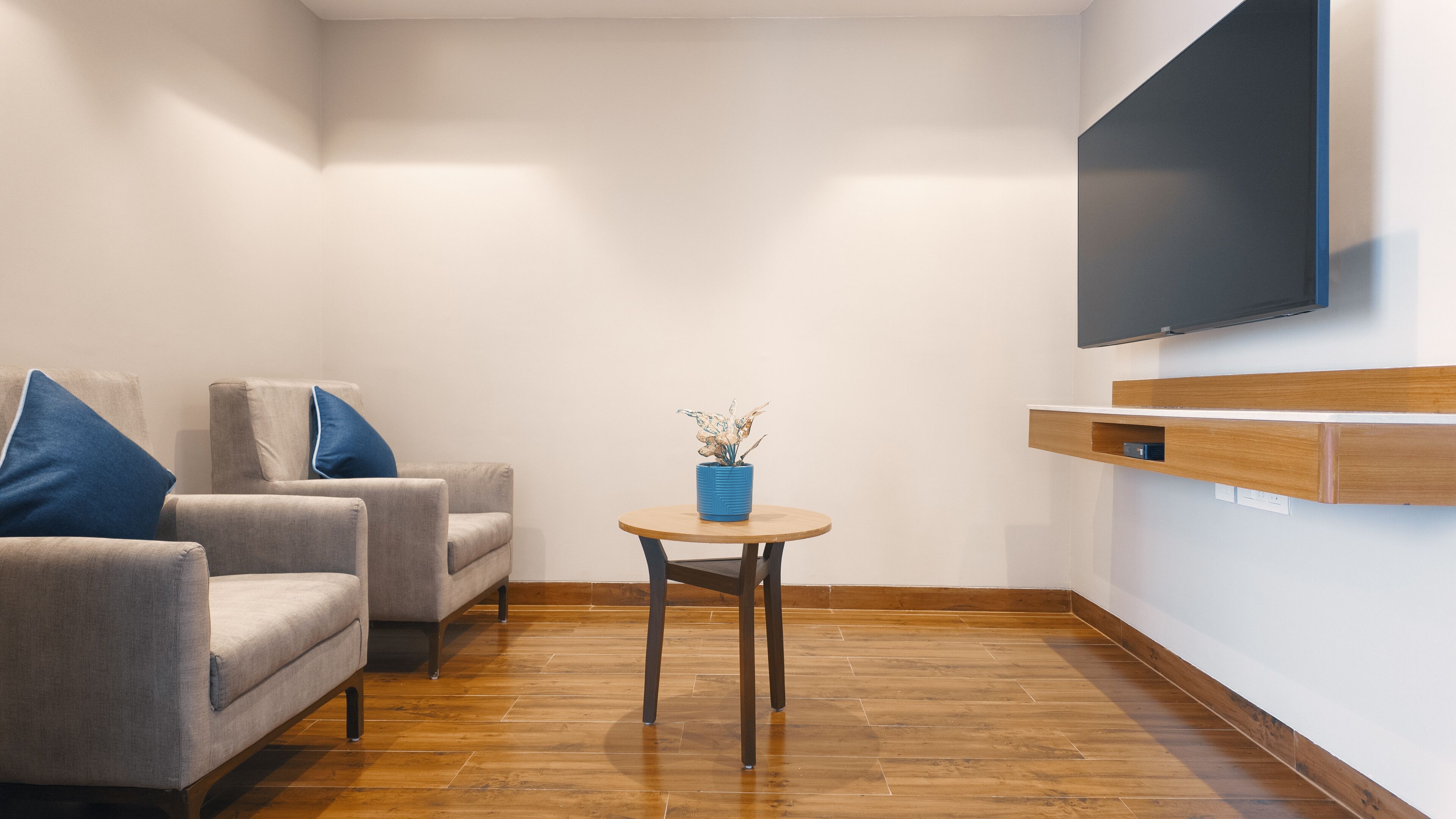 A modern living room with a grey sofa, blue pillows, a small round table with a blue vase, and a mounted TV.