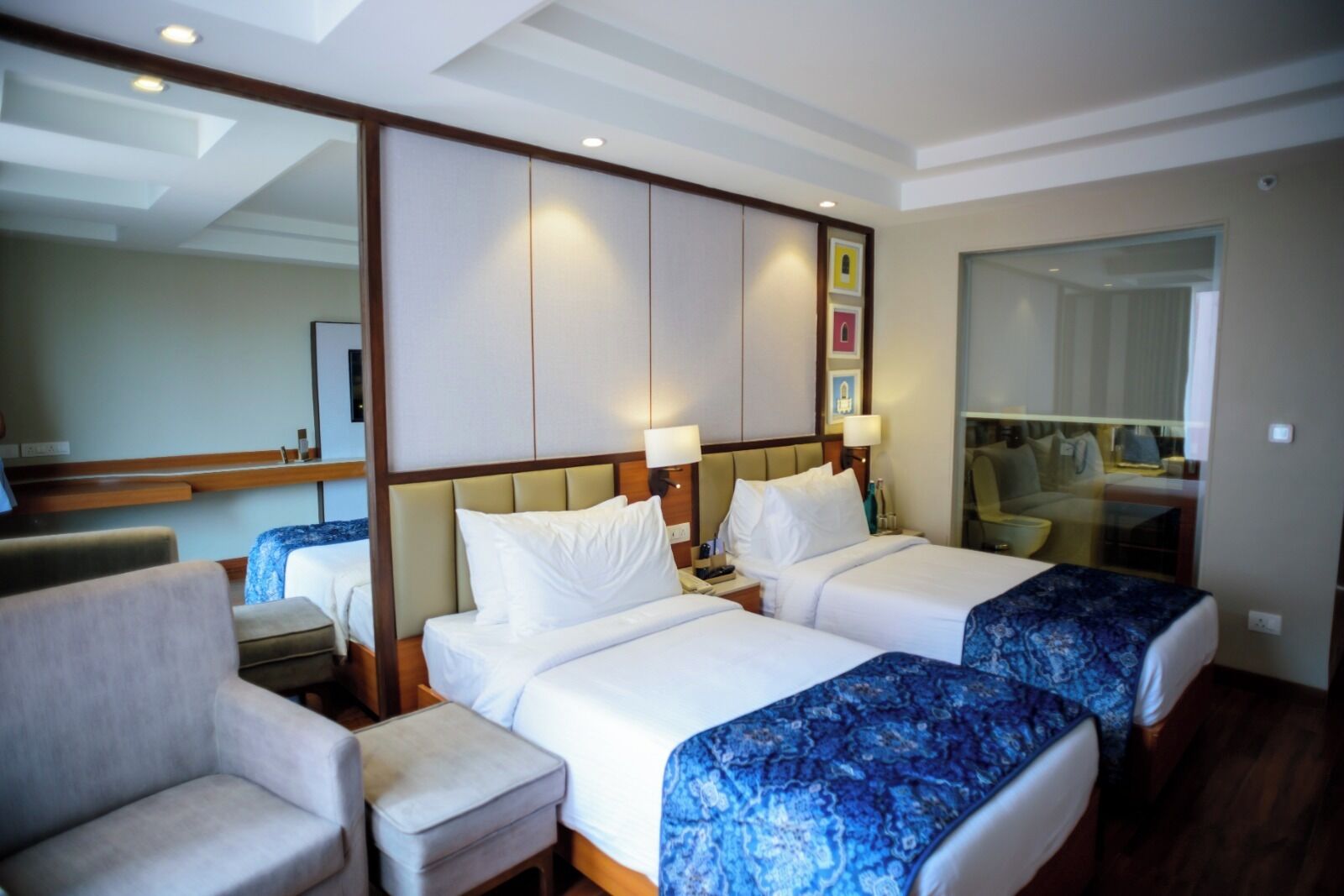 Habitación de hotel con dos camas, un sofá, un escritorio y un espejo grande.