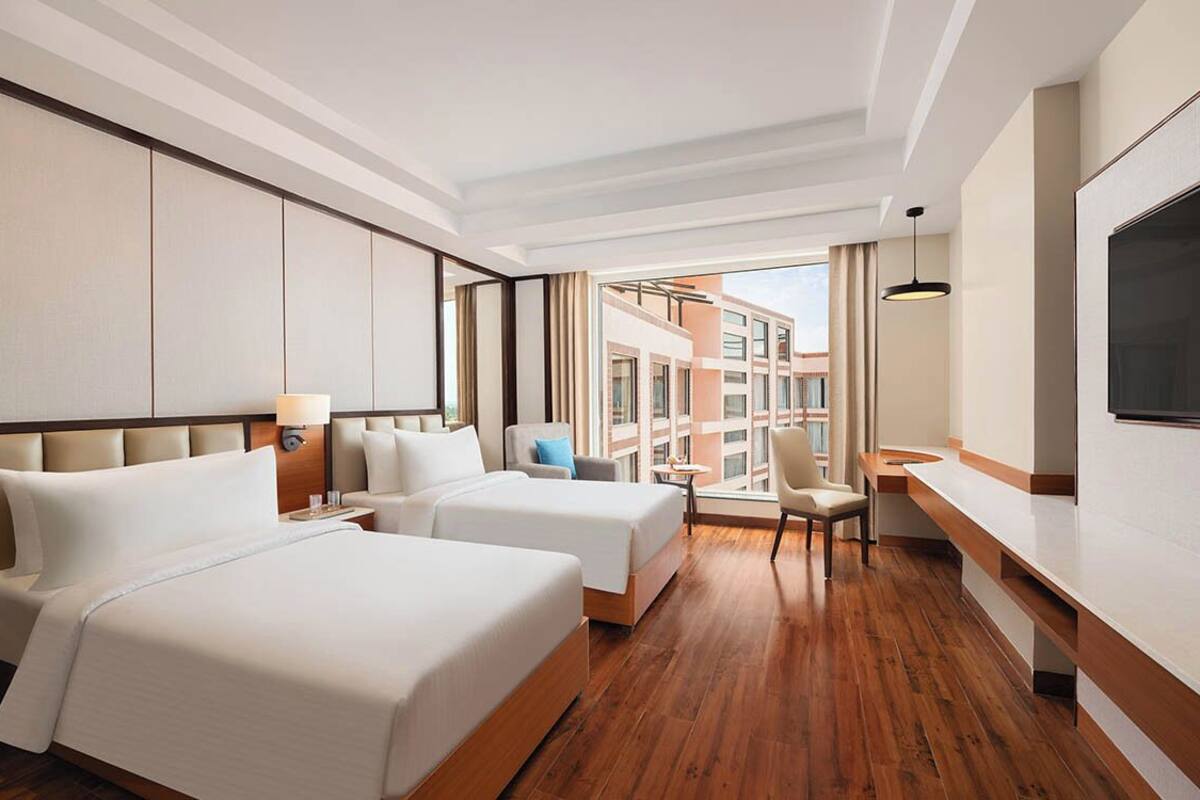A modern hotel room with a large bed, a smaller bed, a desk, and a TV.