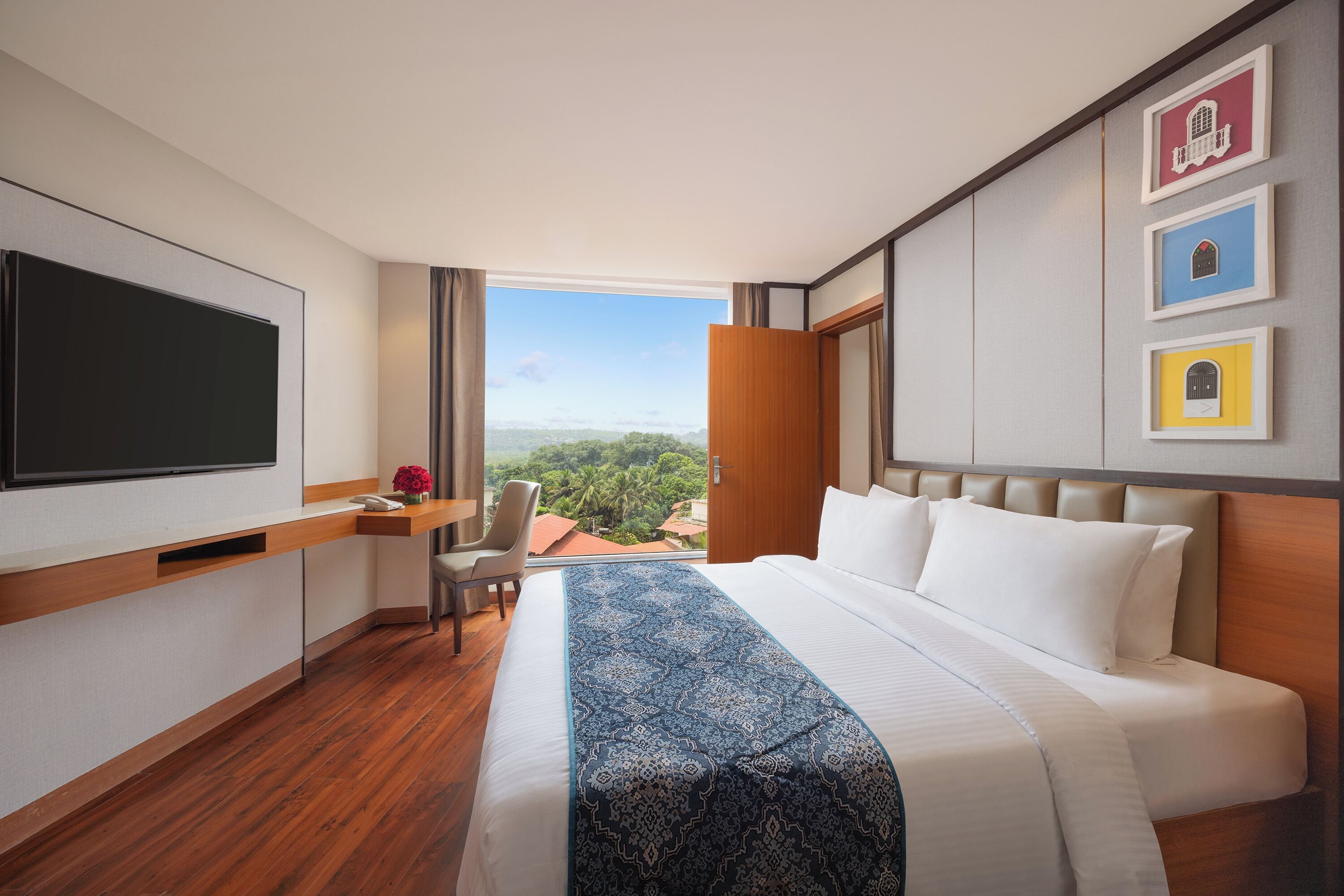 A hotel room with a large bed, a desk with a chair, a flat-screen TV, and framed pictures on the wall.