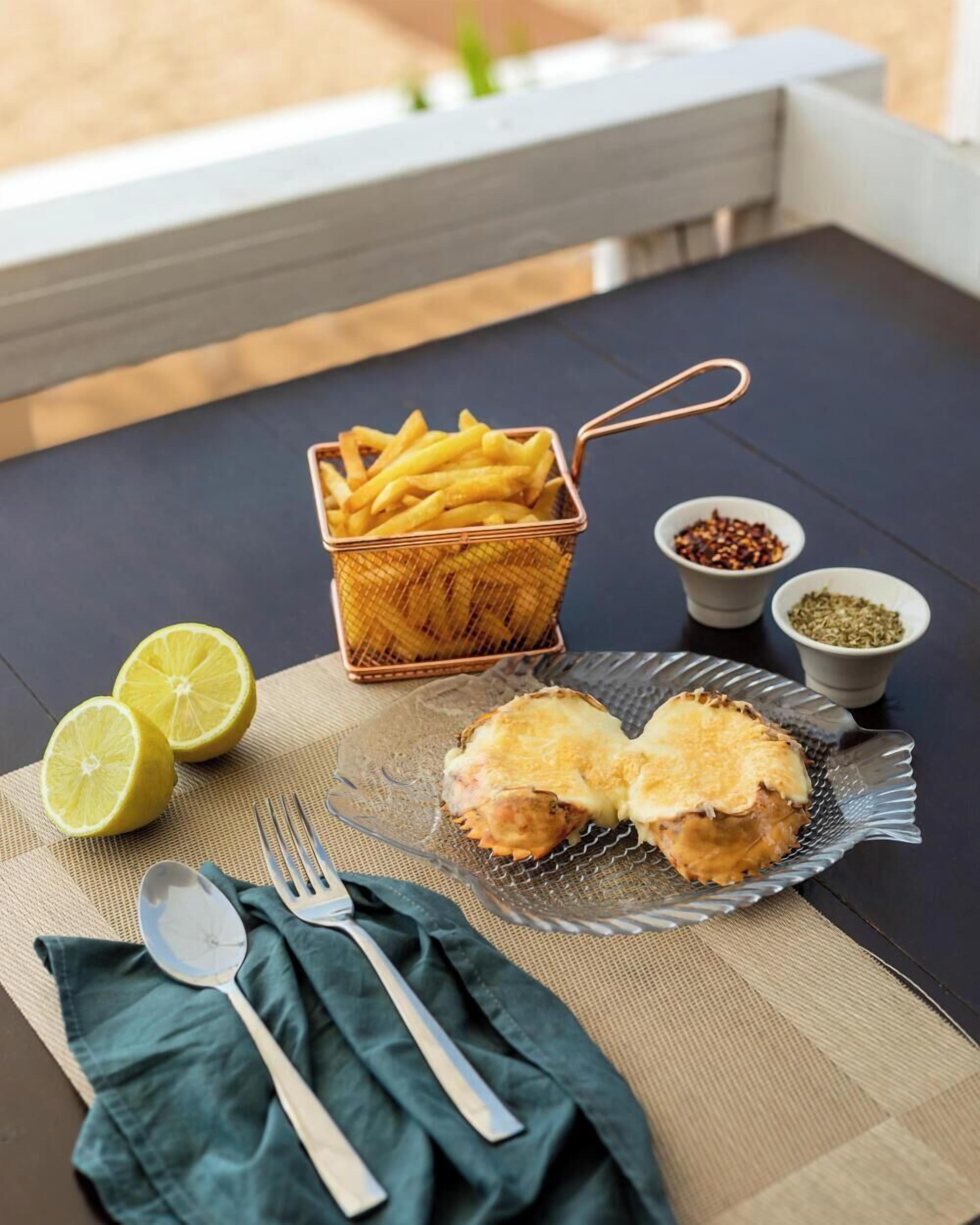 Una mesa con un cesto de papas fritas, mitades de limón, un plato con dos pescados y recipientes pequeños de especias.