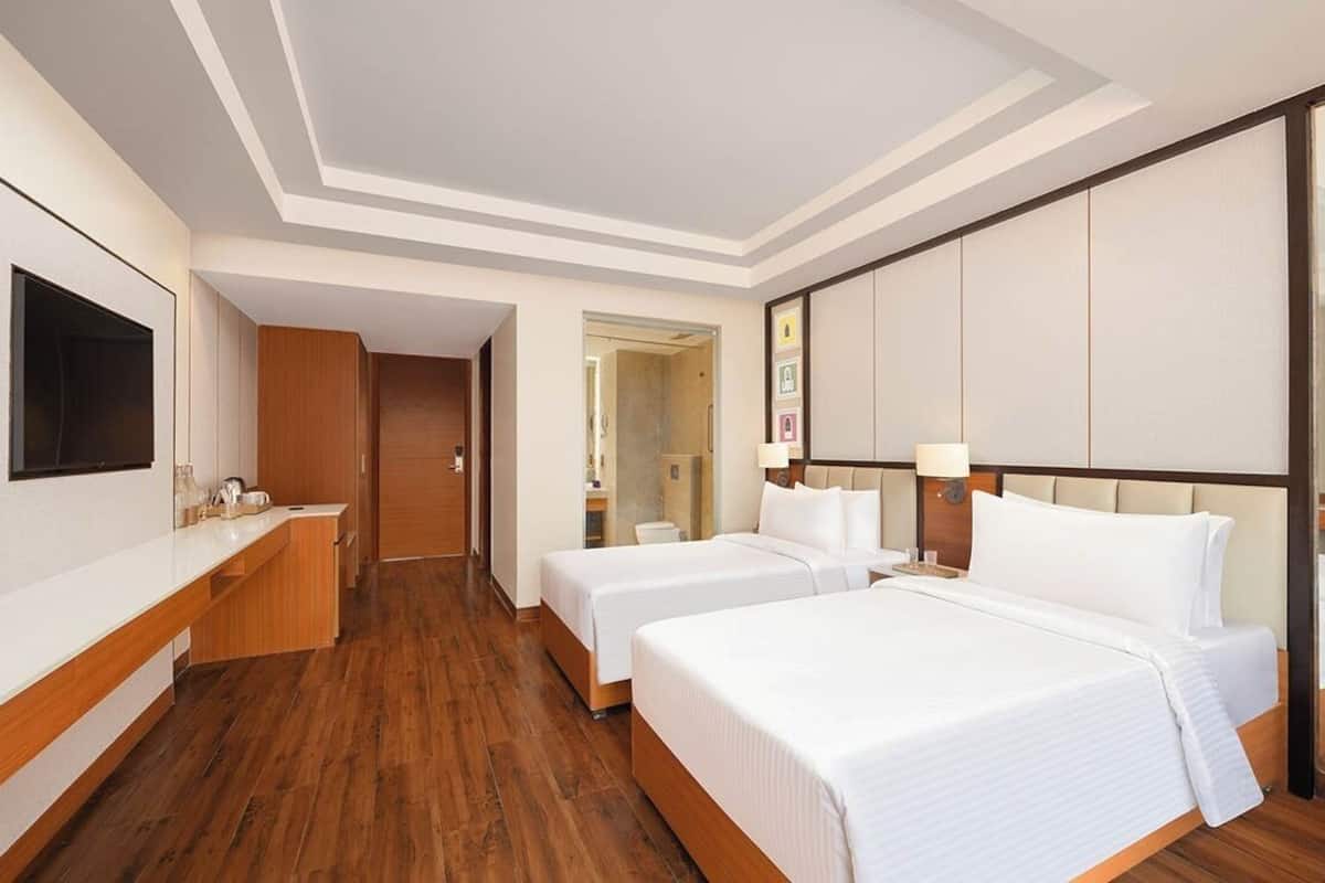 A hotel room with two beds, a TV, a wooden desk, and a large mirror.