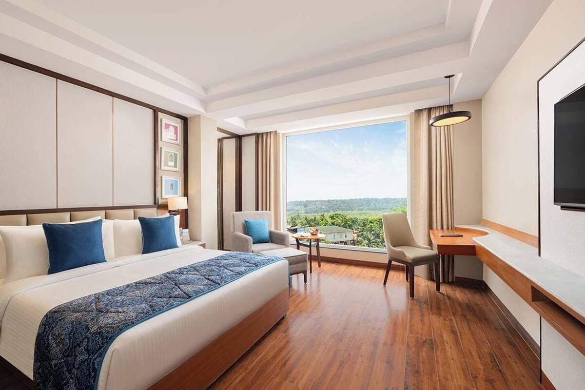 A hotel room with a large bed, a desk, a chair, and a view of the outdoors.