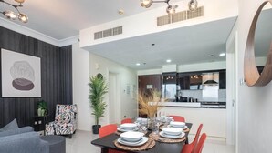 A modern dining area with a black table set for four, surrounded by red chairs. There is a grey sofa and a patterned armchair in the living area, with a large abstract painting on the wall.