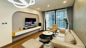 Una sala de estar moderna con un televisor de pantalla plana montado en una consola de madera, un sofá color beige, una mesa de centro redonda y un amplio ventanal con vistas a la ciudad.