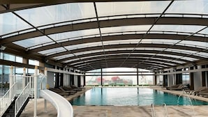Una piscina interior con tobogán, sillas de descanso y vistas a través de amplias ventanas.