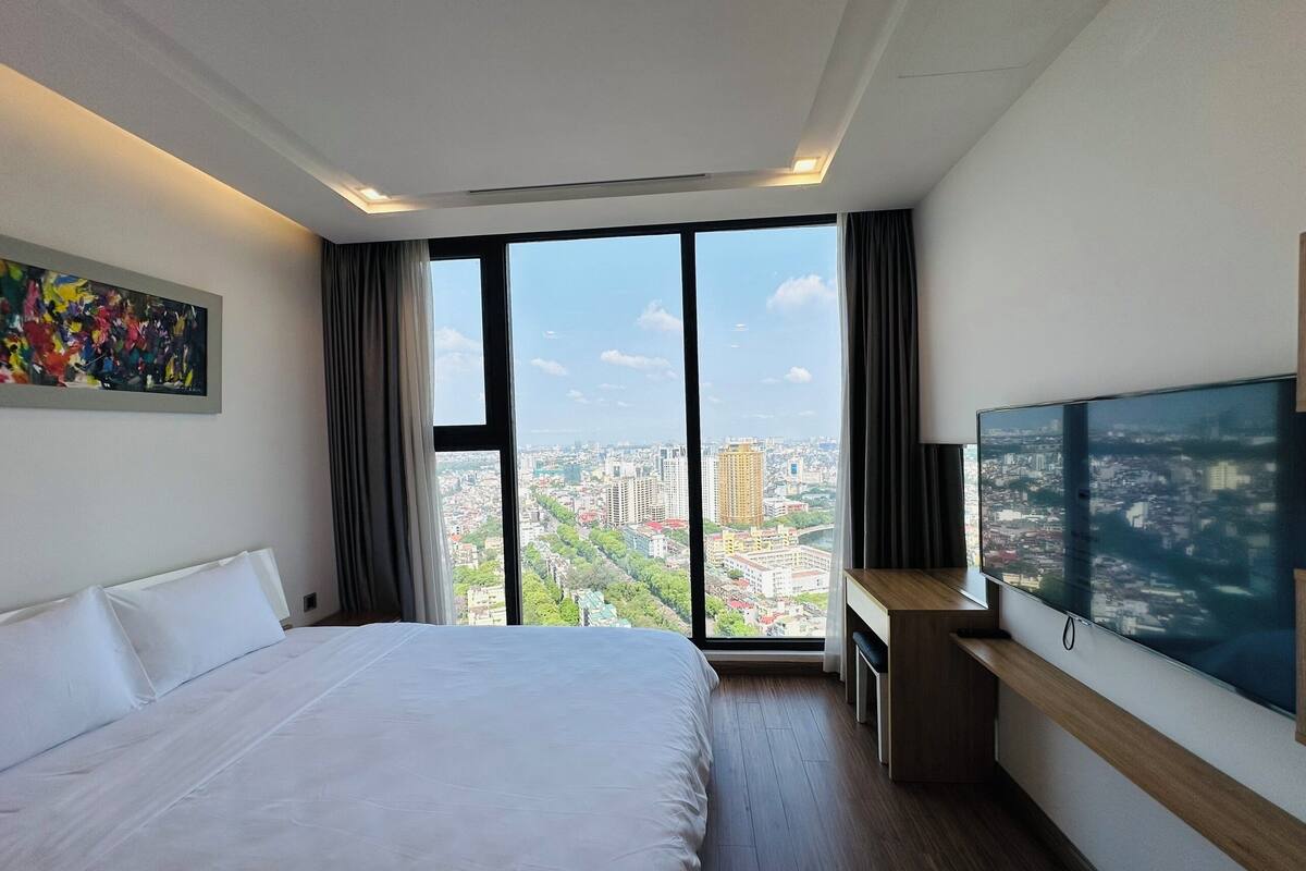 A hotel room with a large bed, a desk, a TV, and a city view.