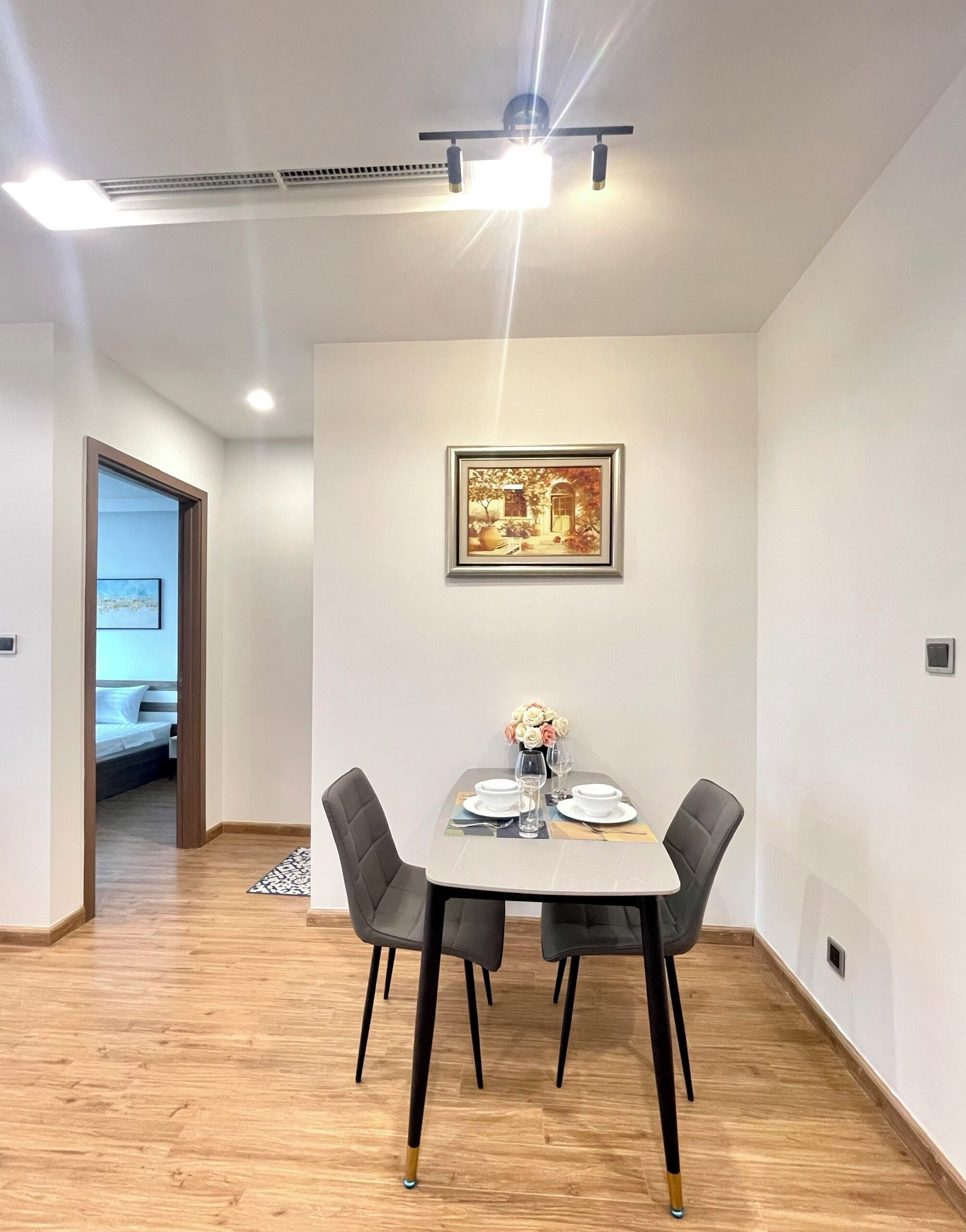 Ein Essbereich mit einem Tisch für vier Personen, zwei Stühlen, einem gerahmten Bild an der Wand und einer Deckenleuchte.