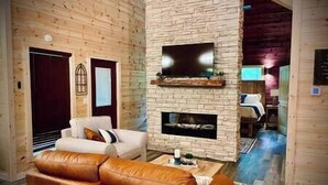 Un salon chaleureux avec une cheminée en pierre, un téléviseur à écran plat fixé au-dessus et un canapé en cuir.