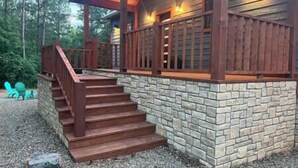 Une cabane en bois avec des fondations en pierre, un escalier en bois et une véranda couverte.
