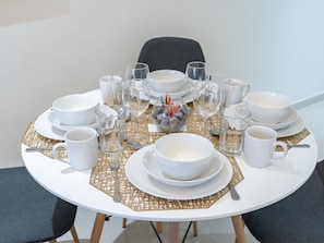A round dining table set with white plates, bowls, and glasses, accompanied by gold-patterned placemats and a decorative centerpiece. - Luxe 1 BR City View Pool & Gym by Belvilla (Dubai)