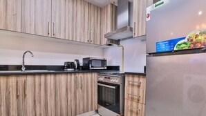 Eine moderne Küche mit Holzausstattung, einem Edelstahlkühlschrank, einer Mikrowelle, einem Wasserkocher und einem Backofen.