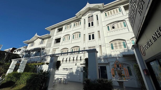 Un bâtiment blanc avec une enseigne indiquant « Nidhra Café » et « Votre hôtel ».