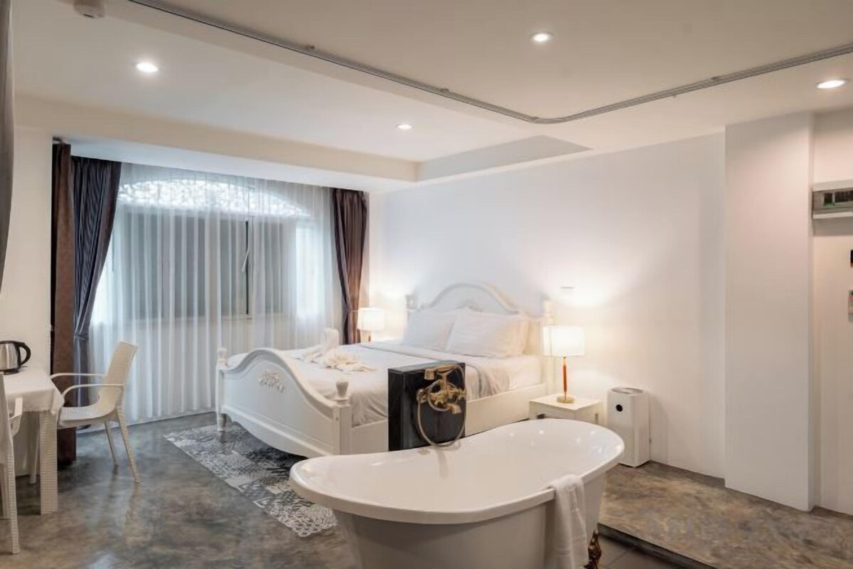 Une chambre d’hôtel moderne avec un grand lit, un coin salon avec un fauteuil, un bureau et une baignoire.