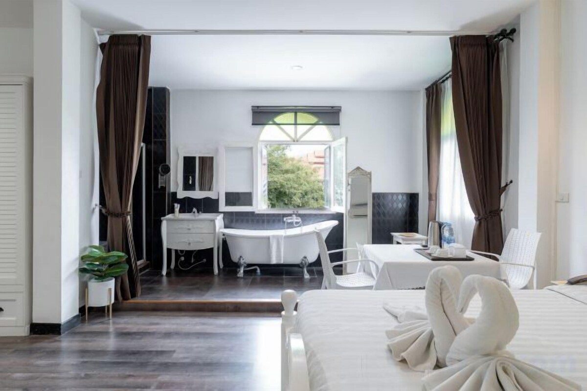 Habitación de hotel con cama, escritorio, silla, baño con bañera y vistas a través de una ventana.