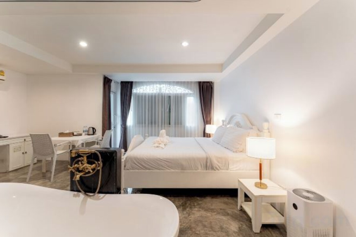 A modern hotel room with a bed, bedside table, lamp, and a desk with a chair.