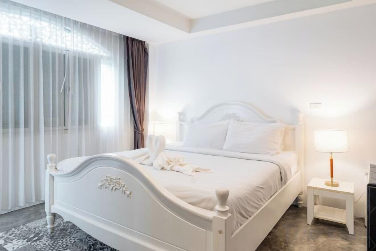 Une chambre d’hôtel avec un lit, une table de chevet avec une lampe et une fenêtre avec des rideaux.
