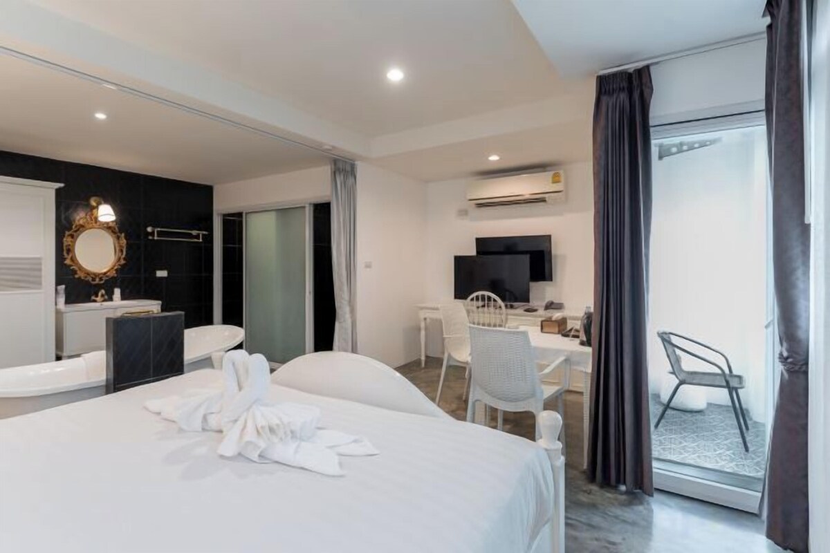 Habitación de hotel con cama, escritorio, silla, televisor y puerta corrediza al exterior.
