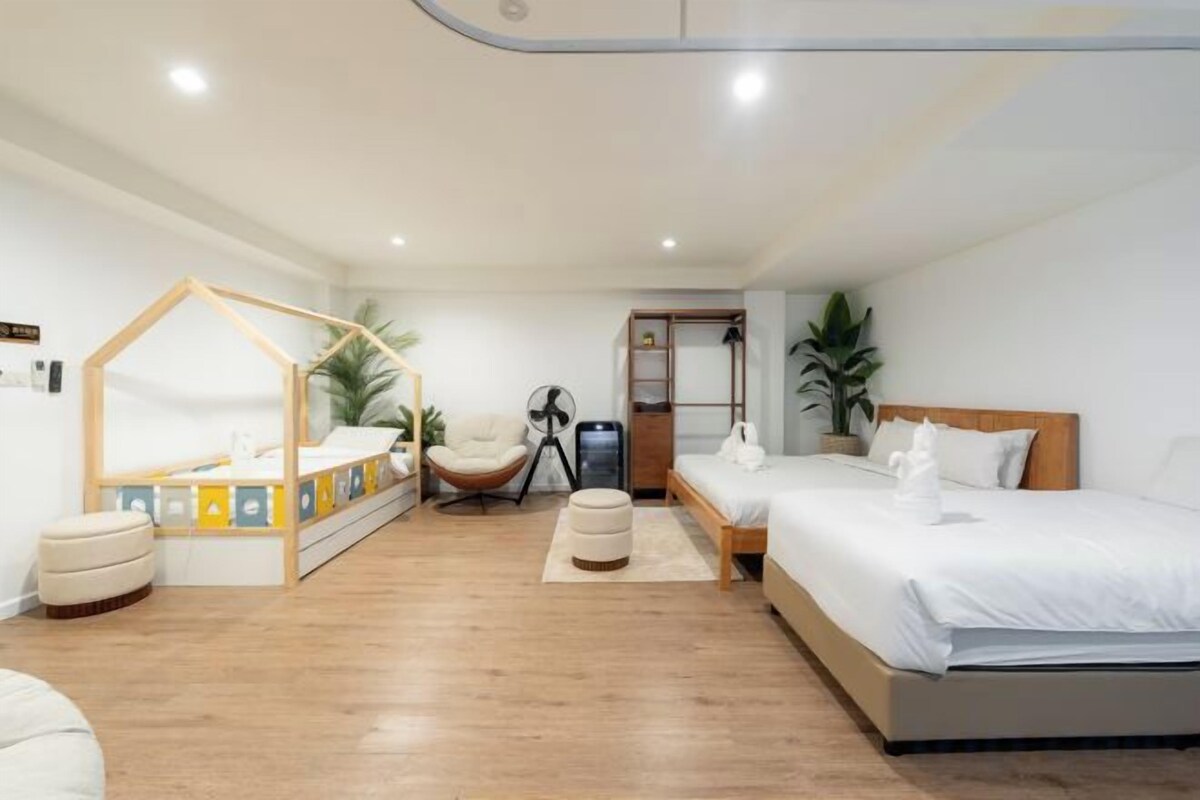 Une chambre avec un plancher en bois, un lit, une banquette, une chaise, un ventilateur et une petite table.