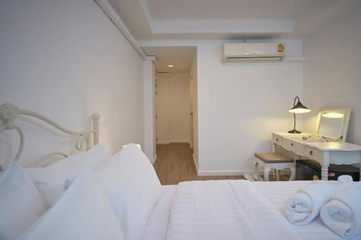 Ett hotellrum med en säng, ett skrivbord med en lampa, en spegel och en resväska.