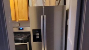 A narrow hallway leading to a kitchen with a stainless steel refrigerator, wooden cabinets, and a built-in oven. - Our cozy apartment is your home away from home. 
 (Hibbing)