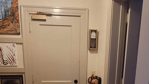 A hallway with a wooden floor, a white door, a rug, a clock, and a framed picture on the wall. - Our cozy apartment is your home away from home. 
 (Hibbing)
