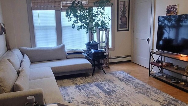 A living room with a sofa, coffee table, TV, and a large window with blinds. - Our cozy apartment is your home away from home. 
 (Hibbing)