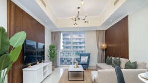 A modern living room with a sofa, a coffee table, a TV, and a large window with a view of buildings. - 2bed Chic Apt Burj Khalifa Gym/pool by Belvilla (Dubai)