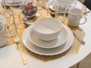Une table dressée avec de l’assiette, des bols et des couverts blancs, le tout posé sur un set de table à motifs dorés.