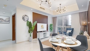 A modern dining area with a round table set for four, surrounded by dark chairs. A television is mounted on the wall, and there is a potted plant on the side. - 2bed Chic Apt Burj Khalifa Gym/pool by Belvilla (Dubai)
