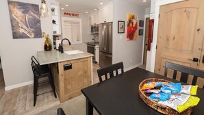 Une cuisine compacte avec un îlot central, un coin repas avec une table noire et un panier de collations posé sur la table.